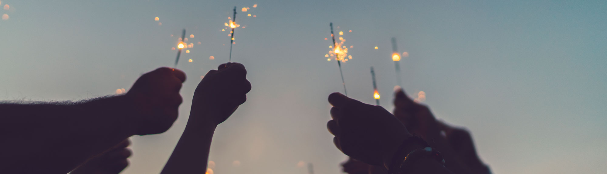 Hände halten brennenede Wunderkerzen in den Abendhimmel